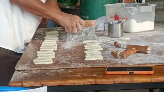 Handmade dumpling dough cutting and folding on floured wooden table with bench scraper and rolling pin, hands shaping and arranging wrappers for food preparation in casual kitchen scene