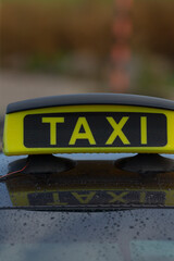 A taxi sign with bright yellow letters stands out on a rainy background, capturing the essence of...