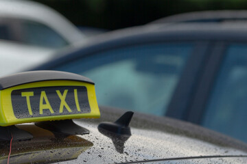 A close-up of a taxi sign on the roof of a car, parked in a busy lot. The sign indicates taxi...