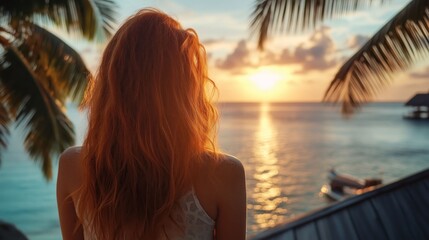 A woman with long red hair watches the beautiful sunset over the ocean from a tropical resort.
