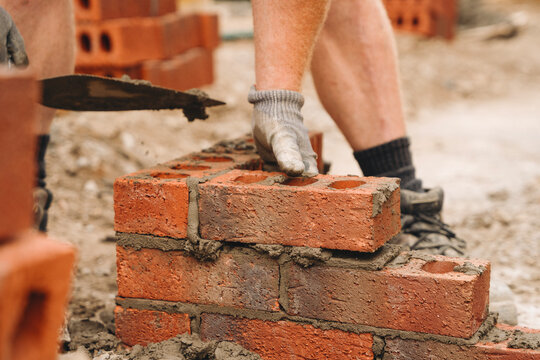 Stone masonry construction in progress with skilled worker laying bricks at a building site during daylight hours