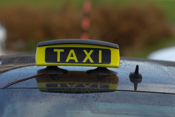 A close-up of a yellow 'TAXI' sign mounted on the rooftop of a taxi vehicle, reflecting its identity as a transportation service.