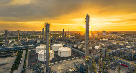 Panorama of an oil refinery and its large storage tanks under a vibrant golden sunset sky,...