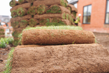 Freshly laid rolls of sod stacked near a home for landscaping in a suburban setting during daylight