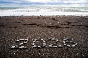 2026 number made of pebbles on sand with stormy sea background, natural texture design for new year celebration, holiday greeting, seasonal decoration, future concept and calendar theme