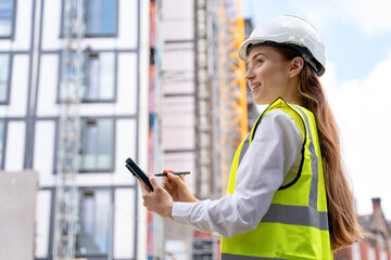 Construction worker assesses project progress on site while wearing safety gear and taking notes in urban environment