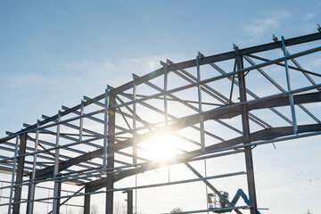 Sunlight shines through the metallic framework of a building under construction in a clear blue sky...