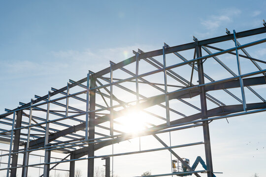Sunlight shines through the metallic framework of a building under construction in a clear blue sky during early morning hours