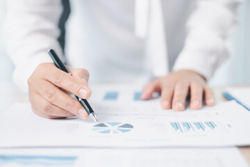 Businessman reviews financial reports, points on chart with pen while analyzing data at office desk...