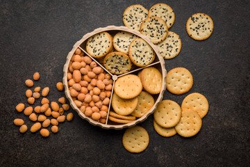 Various salty snacks in a round bowl on black table.