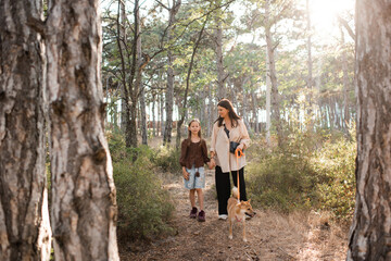 Happy woman and child girl take for a walk shiba inu dog in woods outdoors. Friendship.