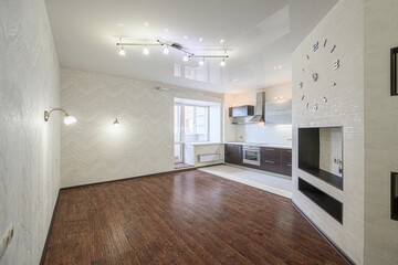 Modern apartment interior with wood floors, textured wallpaper, and an open kitchen. Large clock on brick wall