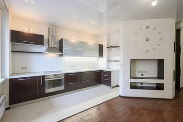 modern kitchen featuring dark wood cabinets, white countertops, and a stainless steel oven. A large wall clock is visible on the brick wall adjacent to the kitchen