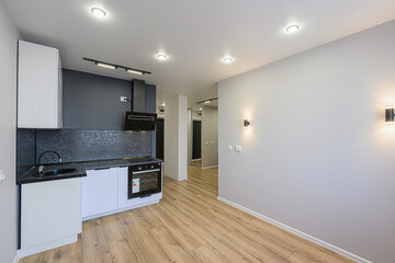 modern, well-lit kitchen space with light gray walls, wooden floors, and white cabinets. A black backsplash complements the kitchen, illuminated by recessed lighting and wall sconces