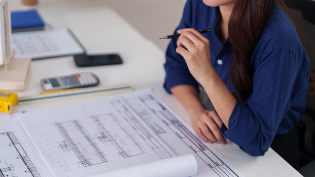 Adult Asian female architect plans building designs office workspace construction blueprints infrastructure projects creative development professional studies