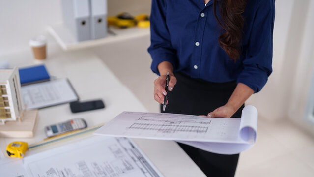 Asian adult architect professional examines building plans in modern office studio for detailed construction project development