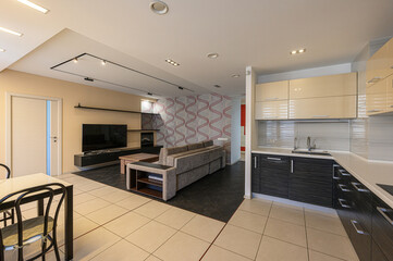 Modern apartment interior with open-plan living, dining, and kitchen areas. Neutral tones and tile flooring prevail