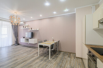 modern apartment interior featuring a dining area with table and chairs, a TV, shelves, and partial view of the kitchen