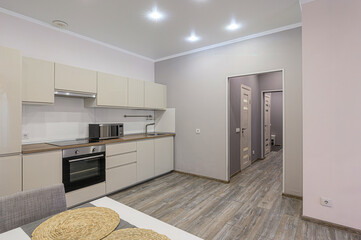 bright, modern kitchen with beige cabinets, stainless steel appliances, and a wooden floor. A...