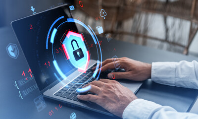 Cybersecurity breach concept showing hands typing on laptop with digital lock icon and futuristic interface graphics over blurred indoor background.