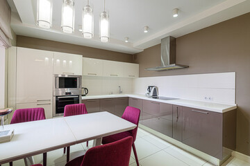 modern kitchen with two-tone cabinetry, white countertops, and bright pendant lighting above a white table with fuchsia chairs