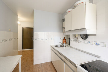 partial view of a kitchen with white cabinets, tiled walls, a sink, and a glimpse into a hallway
