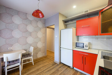 compact kitchen and dining area. Red cabinets contrast with white appliances. Wooden floors and a patterned wallpaper add warmth