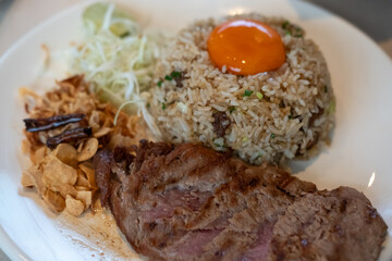 Beef with garlic fried rice, a dish of rice topped with rare beef served with pickled egg yolk with fish sauce on a pan