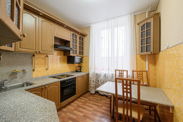 kitchen with wooden cabinets and table, a window covered with a white curtain, a tiled yellow wall