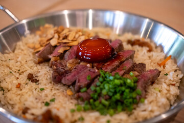 Beef with garlic fried rice, a dish of rice topped with rare beef served with pickled egg yolk with fish sauce on a pan
