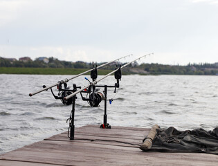 Carp fishing, rod pod with fishing rods on a wooden platform on the lake. Feeder fishing with reel close up. Fishing rods for carp with signaling devices on the holder. World Fisherman's Day. Nature. 