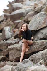 Young pretty long legged brunette woman sitting on rocks by the sea shore 