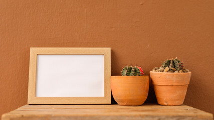 Two terracotta pots hold vibrant cacti, placed alongside a wooden frame ready for a picture. This...