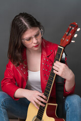 Female guitarist and musician in process of tuning her acoustic guitar, holding it upright and plucking strings in order to ascertain sound of her preferred musical instrument