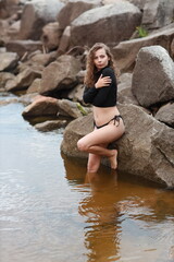Young pretty woman standing in water of sea near big stones