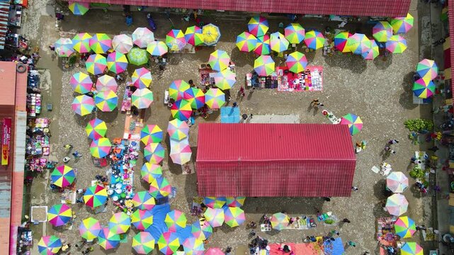 A lively aerial view of the traditional market in Aileu, Timor-Leste. Hundreds of colorful umbrellas belonging to vendors create a vibrant pattern amid the hustle and bustle of buying and selling.