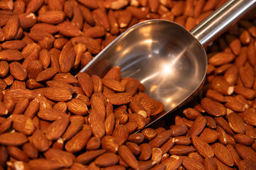Metal scoop surrounded by almonds roasted in paprika spices. Close-up. Background for snacks and...