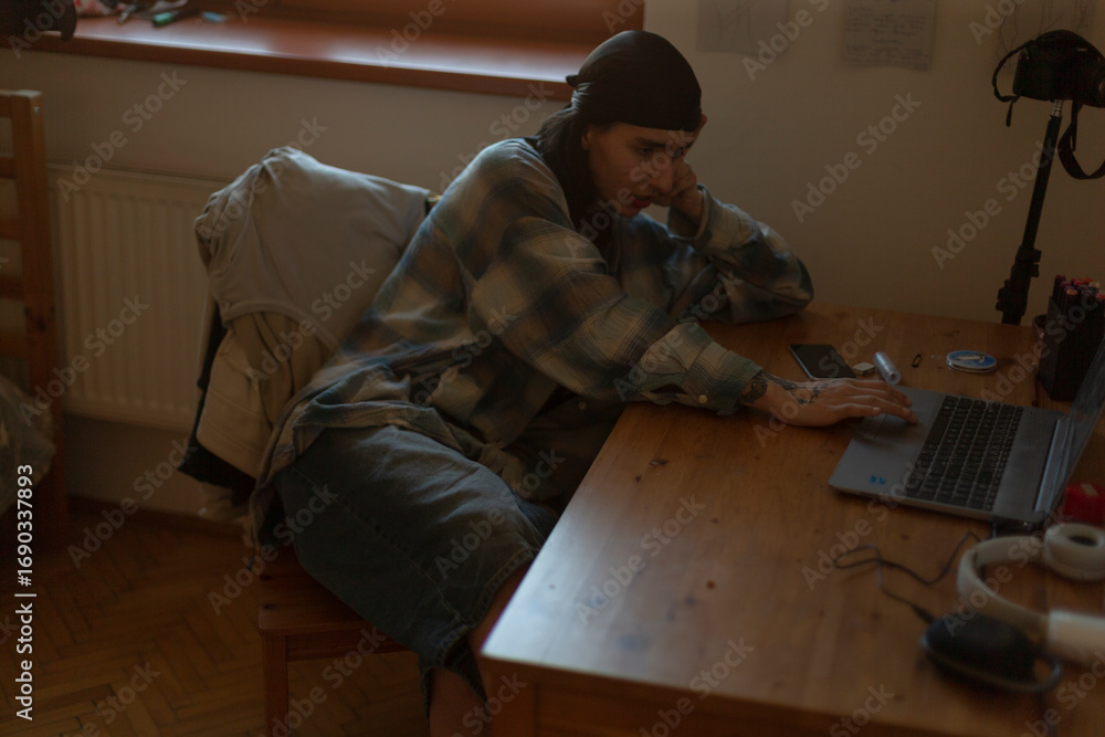 Poster a man is currently seated at a wooden desk while actively using a portable laptop computer for vario
