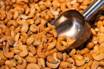 Metal scoop surrounded by roasted cashew nuts. Close-up. Background for snacks and nuts