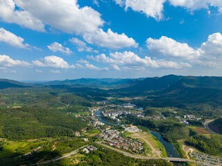 Fototapeta premium China's beautiful landscape unfolds with lush green mountains, a winding river, and a charming town nestled beneath a clear blue sky.