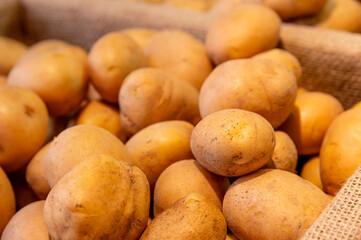 Lots of raw potatoes lying in a tray on the display case of a vegetable shop. Natural not perfect many potatoes. Close-up