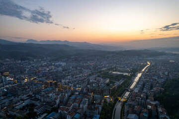 Fototapeta premium Aerial view of Wudang town in China at sunset, showcasing urban landscape with a winding river and distant mountains.