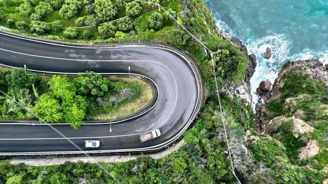Cars driving on a hairpin bend next to a blue-green sea
