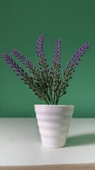 Close-up of a potted artificial lavender plant with green leaves and purple flowers, placed on a table against green background, perfect for decor and lifestyle concepts