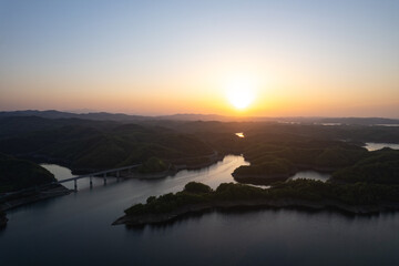 Beautiful sunset paints the sky above Danjiangkou Reservoir, China, illuminating lush green hills and tranquil waters with a golden glow.