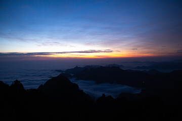 Sunrise light illuminates Wudang Mountain, China, showcasing majestic peaks rising above a soft,...