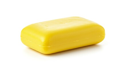 Rectangular yellow bar of soap sits at an angle on a white surface with soft lighting