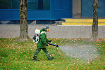 Lawn maintenance worker fumigating grass with backpack sprayer applying pesticide and insect repellent to eliminate harmful ticks mites and mosquitoes ensuring outdoor safety and protection
