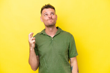 Young caucasian handsome man isolated on yellow background with fingers crossing and wishing the...