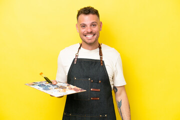 Young artist caucasian man holding a palette isolated on yellow background with surprise facial...